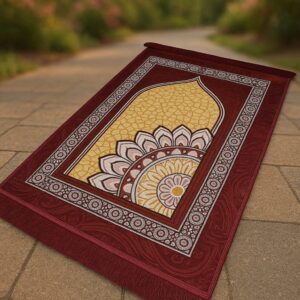 Elegant maroon and gold Islamic prayer mat (jayenamaz) with a central mihrab design and floral mandala pattern, laid out on a paved path.